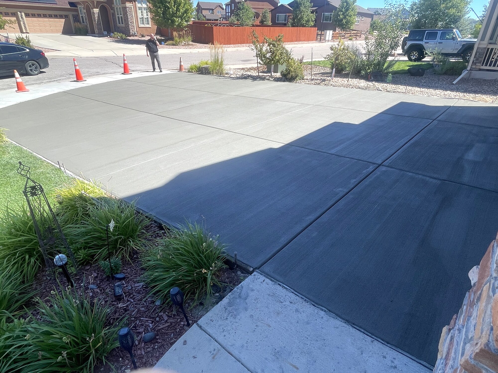 Fresh dark-gray broom-finished concrete driveway at a landscaped home in Colorado Springs.