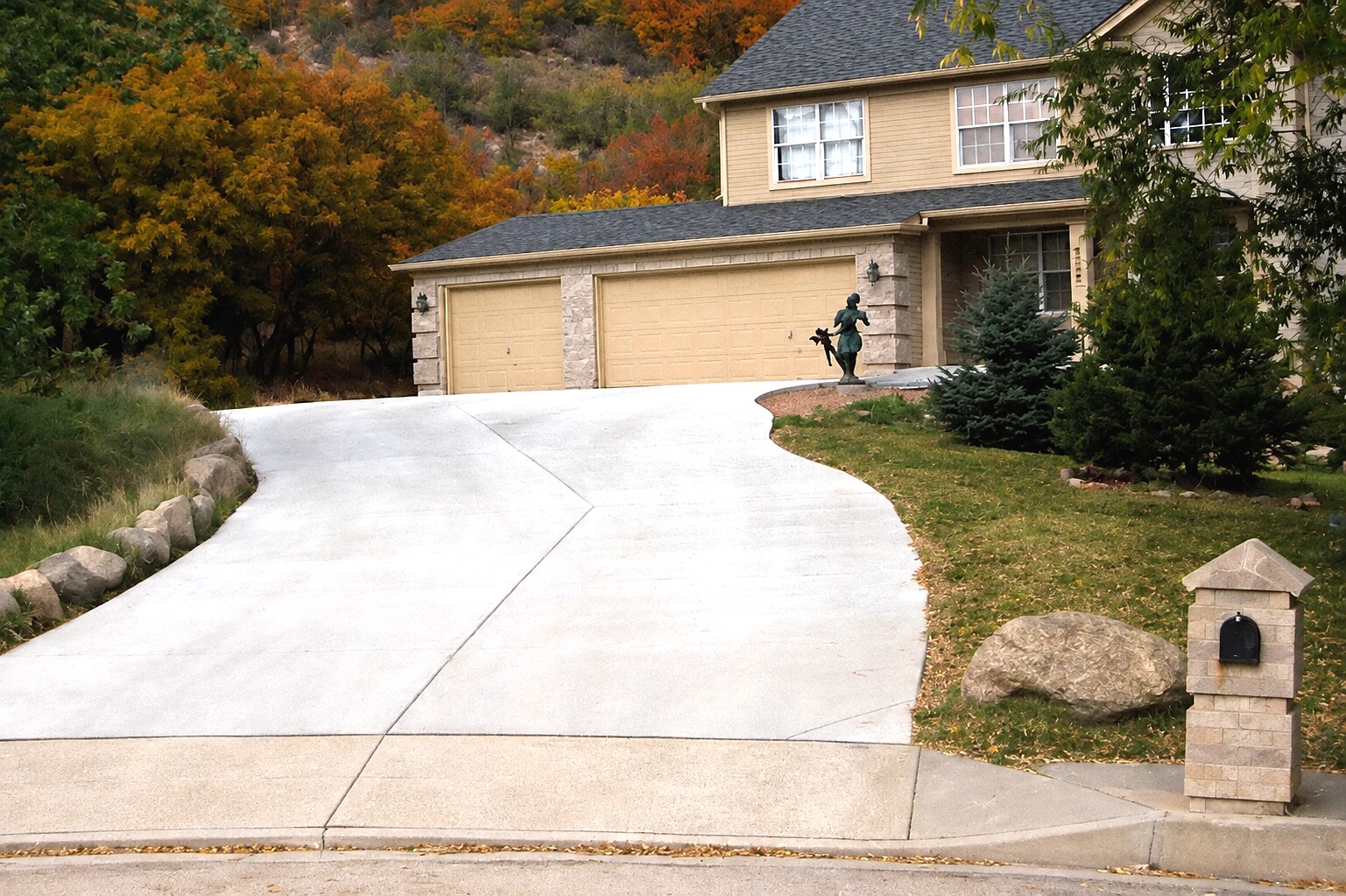 Curved light-gray concrete driveway leading to a hillside Colorado Springs home.