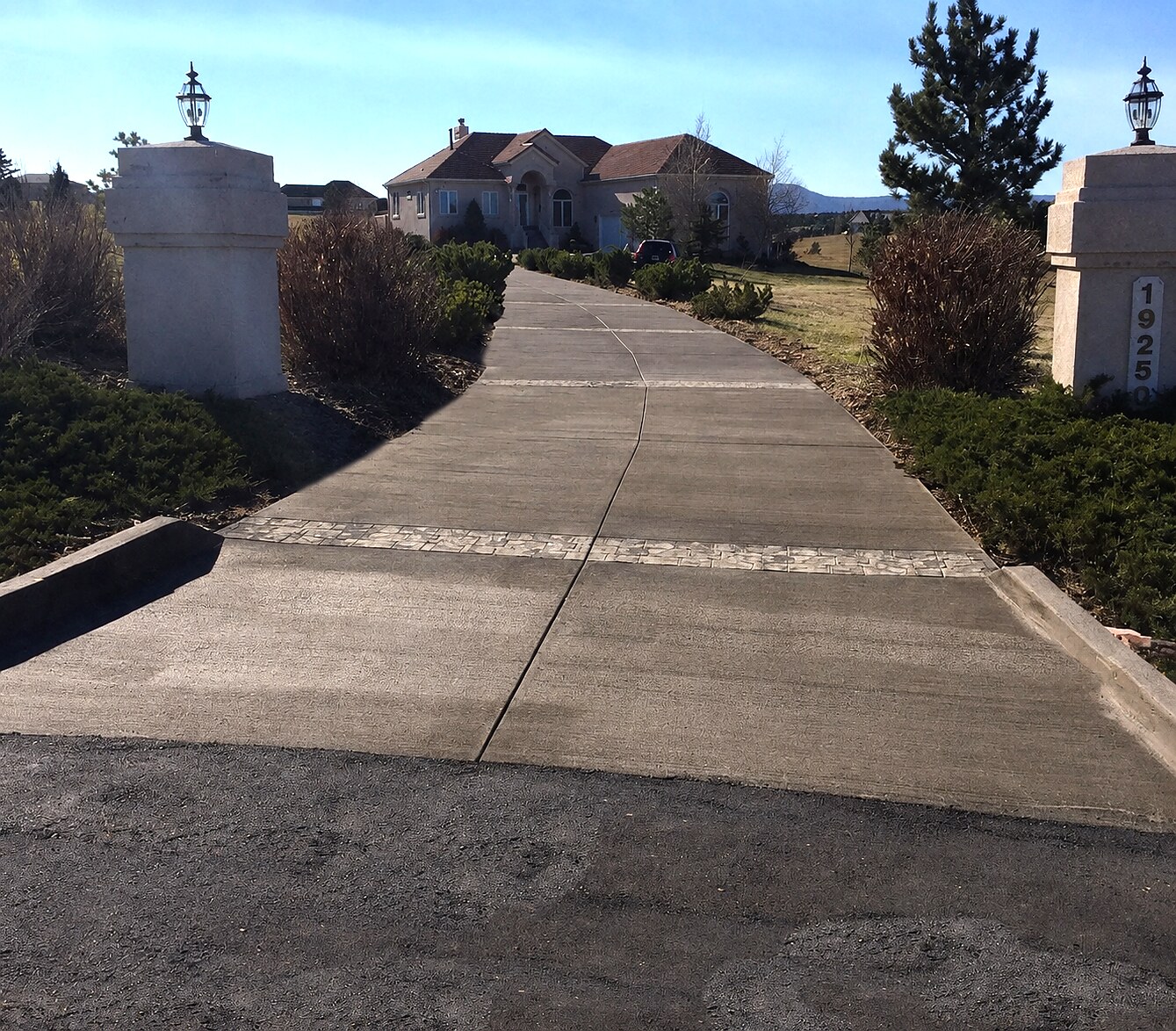 Long colored concrete estate driveway between masonry entry pillars in Colorado Springs.