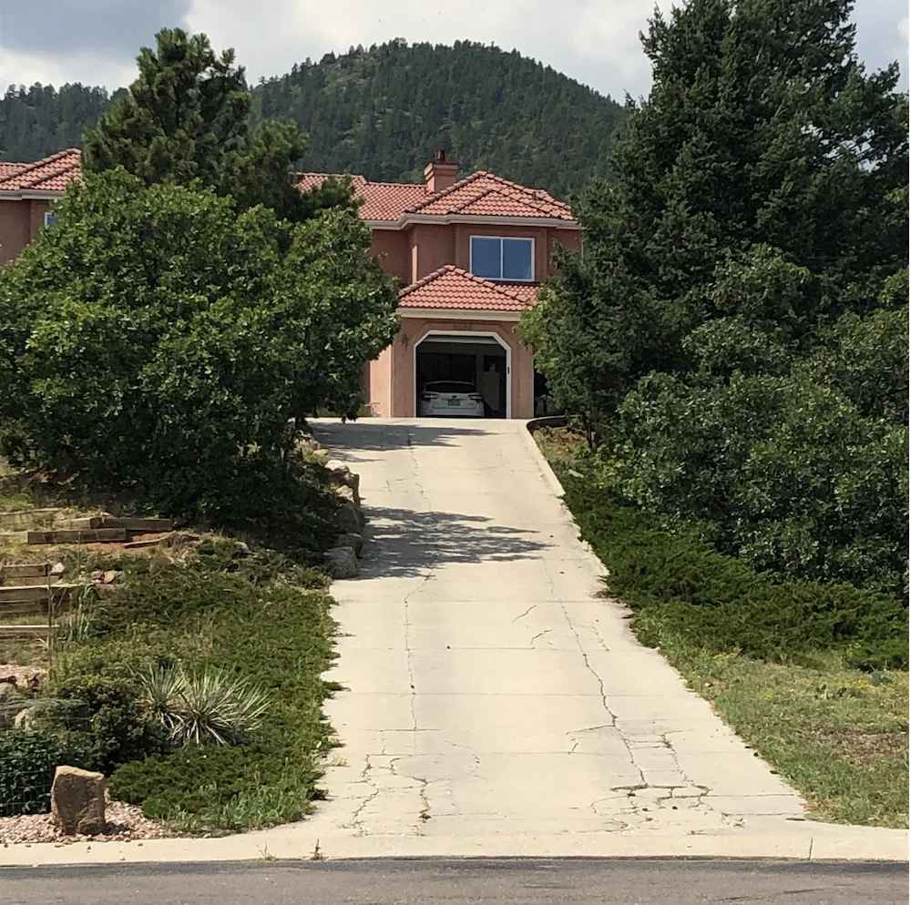 Concrete driveway with repair and resurfacing needs on a Colorado hillside home