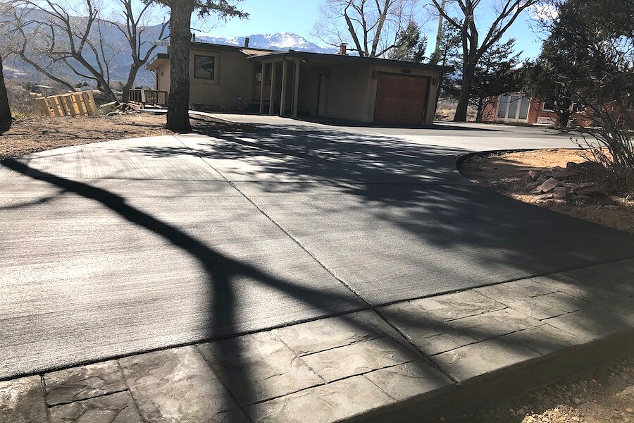 Broom-finished concrete driveway beneath mature trees in Colorado Springs.