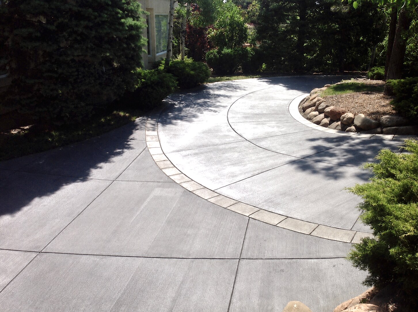 Curved gray concrete driveway with a decorative border and landscaping in Colorado Springs.